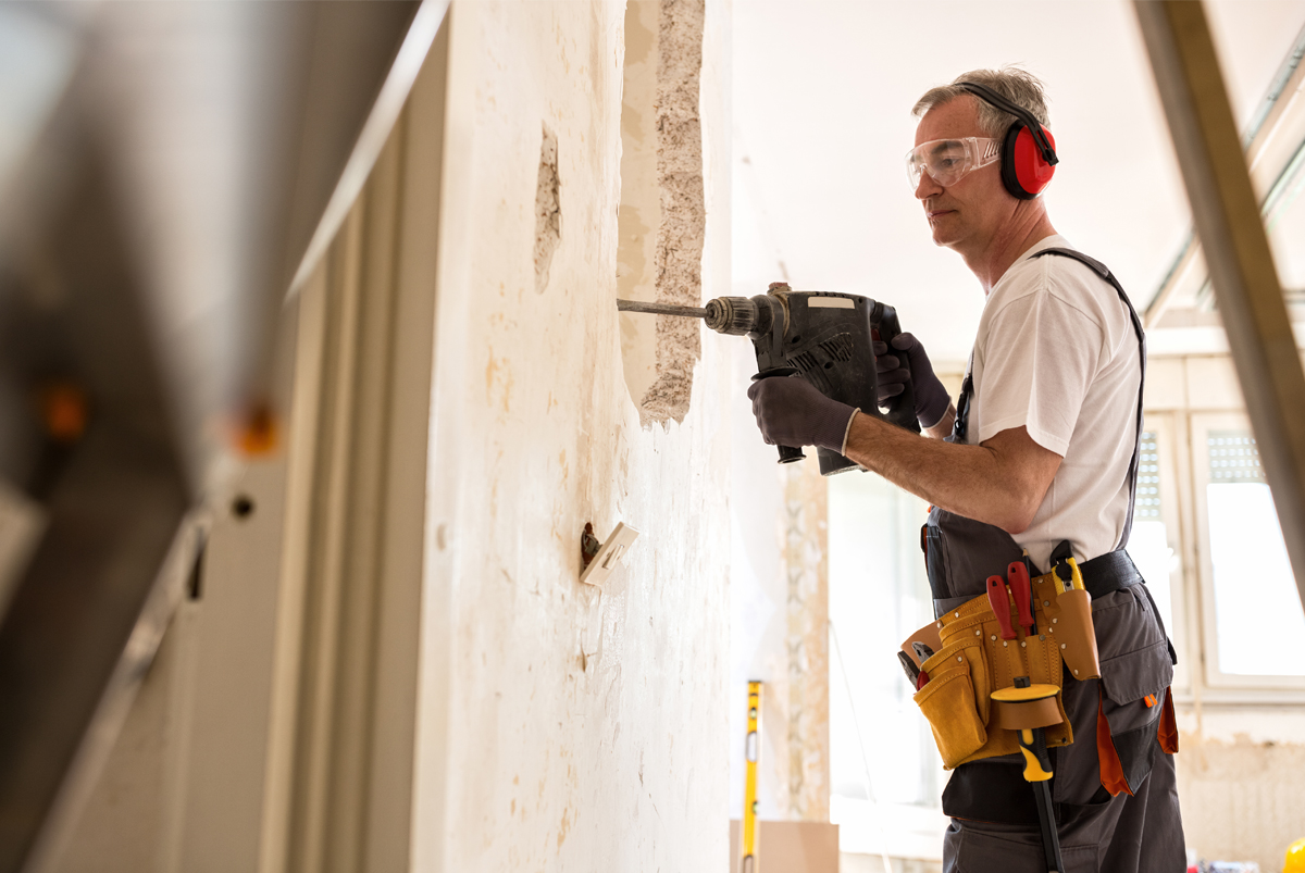 A worker with a hammer drill, ear protection and a tool belt on a renovation job