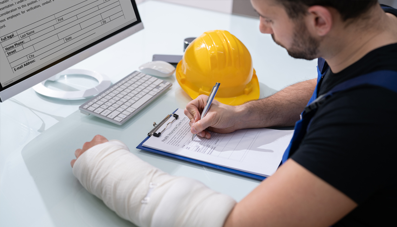 A worker with a bandaged arm fills out a claim form beside a yellow hard hat
